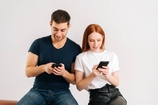 istock Studio portrait of happy addicted couple using browsing mobile phone looking at screen sitting on white isolated background. 1366462750