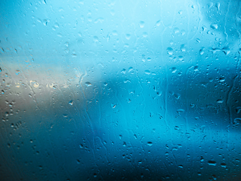 blue and white lights from the surroundings fall into the window pane, which is wet and steamed up by raindrops. the focus is on the foreground