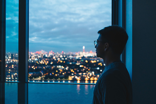 He relaxes at home, looking out across water to city lit up before dawn