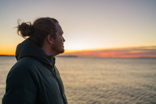 istock Young man relaxes by the sea at sunrise 1366464536