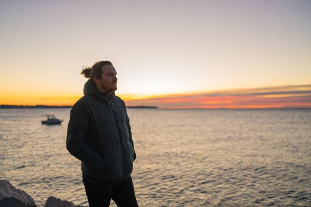 istock Young man relaxes by the sea at sunrise 1366464599