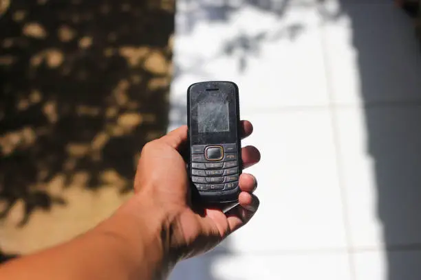 Photo of Hand holding an old used cell phone with conventional keypad that were popular in the late 90s and 2000s
