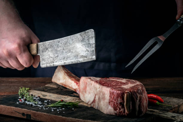 istock A butcher cuts beef Tomahawk steak on a bone with a cleaver on a wooden cutting Board on a dark background 1366465424