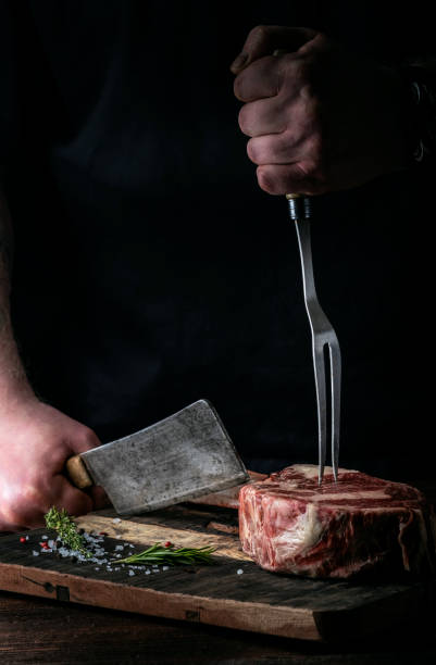 istock A butcher cuts beef Tomahawk steak on a bone with a cleaver on a wooden cutting Board on a dark background 1366465442