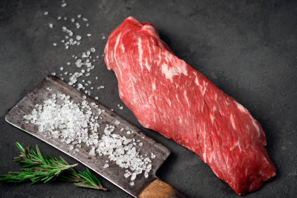 Raw tenderloin of beef or skirt steak with a hatchet for meat, salt and rosemary on a dark stone background, close up Raw tenderloin of beef or skirt steak with a hatchet for meat, salt and rosemary on a dark stone background, close up flank steak stock pictures, royalty-free photos & images