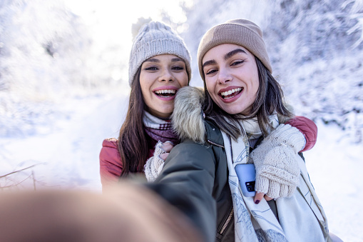 Photo of two young girls having fun and make a selfies on the snow in nature.