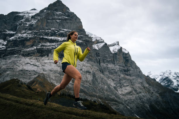 une femme athlétique court à travers les alpes suisses au début de l’automne - cross coat photos et images de collection