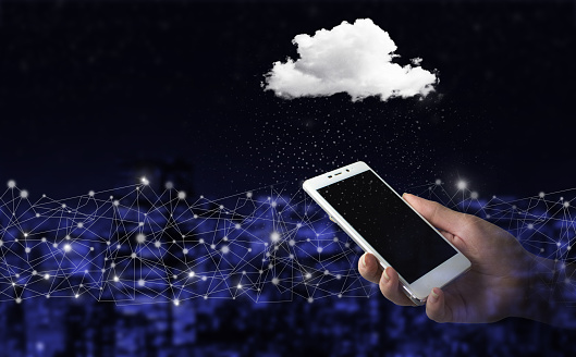 Cloud computing technology internet concept background. Hand hold white smartphone with digital hologram cloud sign on city dark blurred background. Modern cloud technology. Integrated digital web.