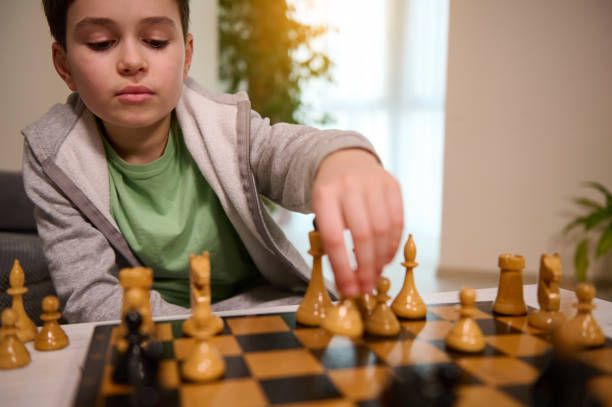 istock Portrait of a concentrated handsome smart boy picking up a chess piece while making move on chess board. Chess game for clever mind, kids intellectual entertainment and logic development concept 1366472606