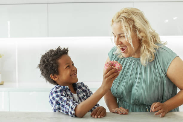 mom and her child boy with black hair eating donut in the kitchen to mothers day - family large american culture fun imagens e fotografias de stock