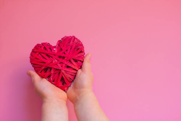 istock baby's hands holding red wicker heart on pink background with copy space 1366477548
