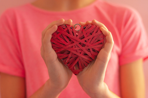 girl's hands hugging a wicker red heart