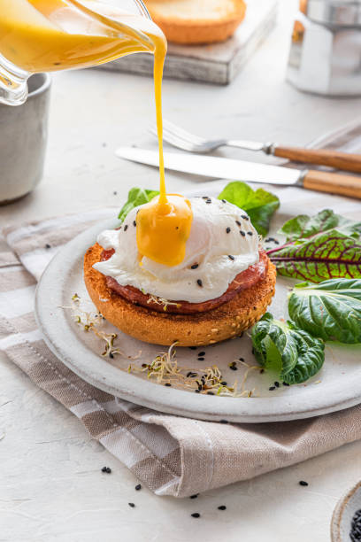 pouring hollandaise sauce over poached egg for cooking benedict egg for tasty breakfast. vertical orientation - hollandaise sauce imagens e fotografias de stock