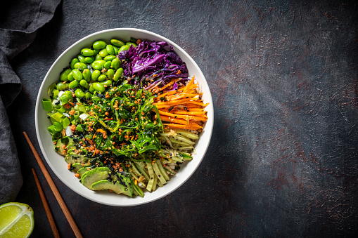 Sushi bowl also Poke bowl vegan plant based asian recipe with ingredients as sushi rice, edamame, wakame seaweed salad, red cabbage, avocado, cucumber, carrot, red onion, soy sauce, sesame oil, maple syrup, lime, garlic
