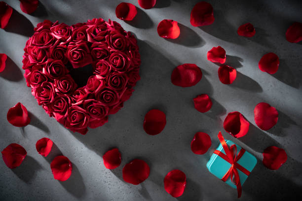 istock Valentines red rose flower petals heart shape on gray copy space and gift box 1366480082