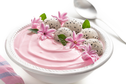 Pitahaya and strawberry yogurt breakfast bowl with mint leaves and pink flowers decoration isolated on white, dragonfruit pitaya