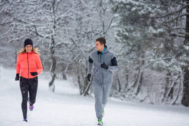 istock A young couple is running in a forest on a cold winter day. 1366480215