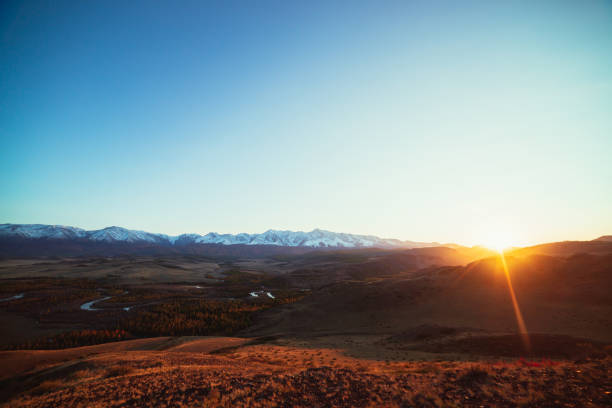 paysage d’automne impressionnant avec rivière de montagne dans la vallée forestière et grande chaîne de montagnes enneigée dans les rayons du soleil doré. vue spectaculaire de la colline aux montagnes enneigées et à la vallée d’automne en rayo - russia river landscape mountain range photos et images de collection