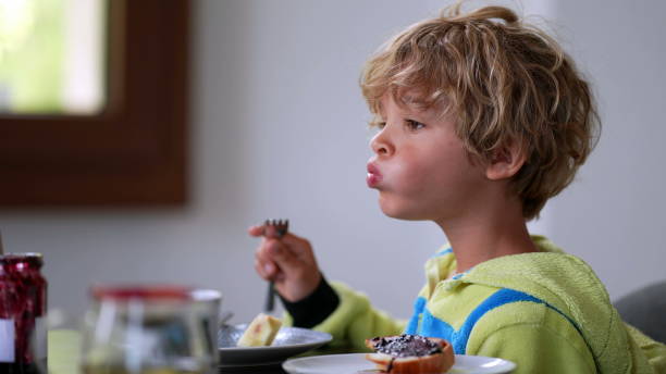 istock Pensive child sitting at breakfast table eating fruit. Thoughful boy 1366484550