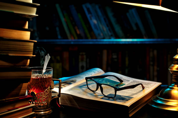 Library. A book unfolded under a desk lamp, with simple black glasses on it.