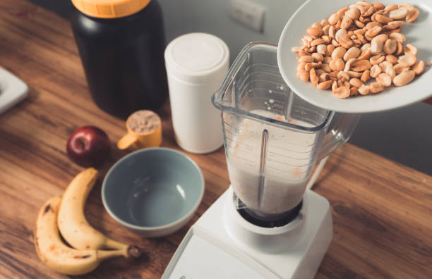 zubereitung eines protein-smoothies durch zugabe einer tasse gerösteter erdnüsse - ground nuts stock-fotos und bilder