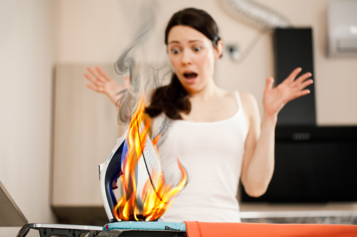 A woman screams in panic when she sees a burning iron. Causes of ignition and fire in housing. Fire safety and fire extinguishing