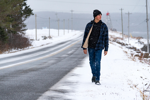 A male teen walking on a country road in a snow storm