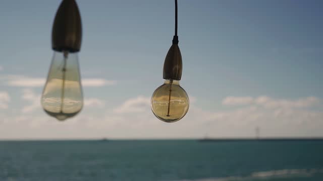 Two light bulbs hang on wires against the background of a beautiful sea. The seascape is reflected in the light bulbs