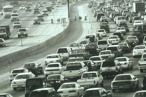 Car and trucks plow their way through the late afternoon rush hour on a southern California freeway.  Photogrpahed with a black and white transparency film the grain inherent in the film lends to the grittiness.