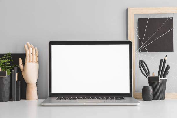 istock Laptop white screen at home office desk with supplies and grey wall. Minimalistic workspace. 1366498624