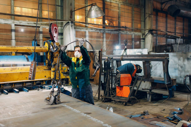 istock Worker lift metal sheet with crane chain hoist with remote controller and hook at industrial factory plant. 1366500509
