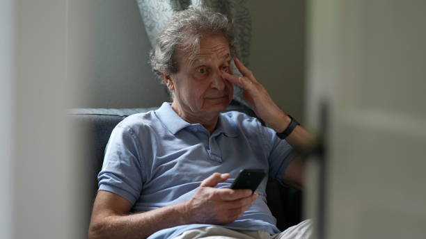 istock Pensive senior man sitting on sofa looking at cellphone device, person scratching eyes 1366500721
