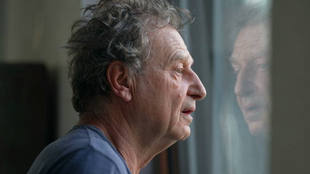 istock Pensive senior man standing by window looking outside. Thoughtful old person 1366502446