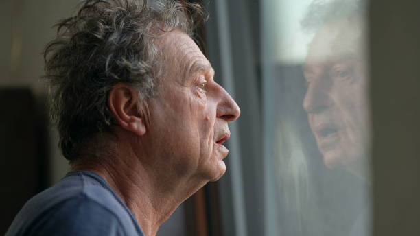 istock Pensive senior man standing by window looking outside. Thoughtful old person 1366502479