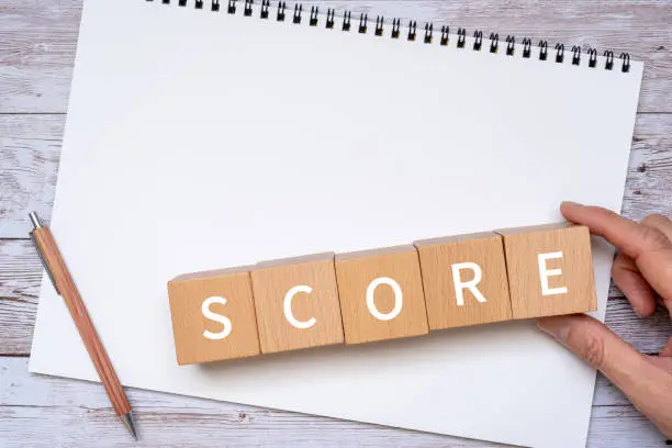 Wooden blocks with "SCORE" text of concept, a pen, a notebook, and a hand.