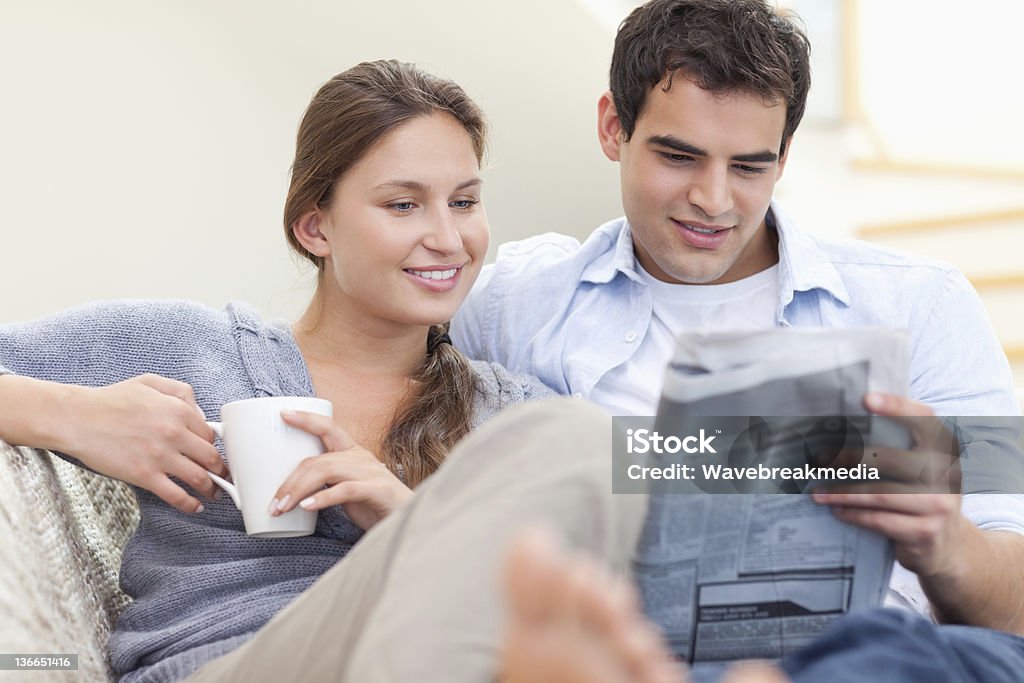 Pareja leyendo las noticias mientras están recostadas en un sofá - Foto de stock de Leer libre de derechos