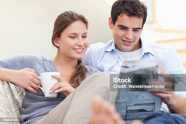 Pareja Leyendo Las Noticias Mientras Están Recostadas En Un Sofá Foto de stock y más banco de imágenes de Leer