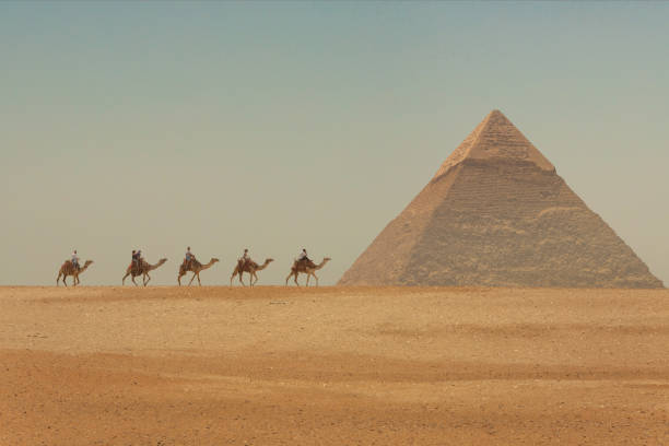 touristes à dos de chameau devant les grandes pyramides d’égypte - giza pyramids egypt north africa africa photos et images de collection