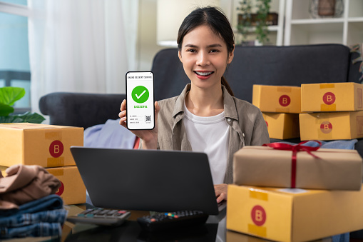 Startup small business, woman hand using smartphone with scan QR code on cardboard box delivery for products to send to customers.