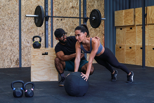 Trainer helping woman to do abs training inside a gym GYM