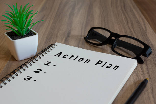 istock Action plan text on white notepad with potted plan, glasses and a pen on wooden desk 1366535292