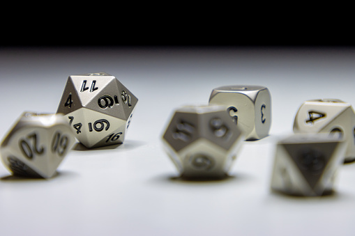 A set of assorted metal fantasy role playing game dice laying on a white surface.