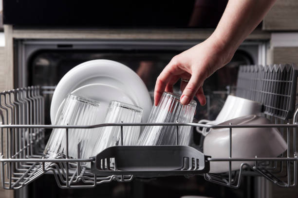 Open dishwasher with clean cutlery, glasses, dishes inside in the home kitchen Close-up of female hand loading dished to, empty out or unloading from open automatic stainless built-in dishwasher machine with clean utensils inside in modern home kitchen. Household domestic life dishwasher stock pictures, royalty-free photos & images