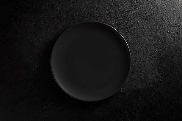 istock Empty black plate on black textured background. Moody, top down view. 1366541066