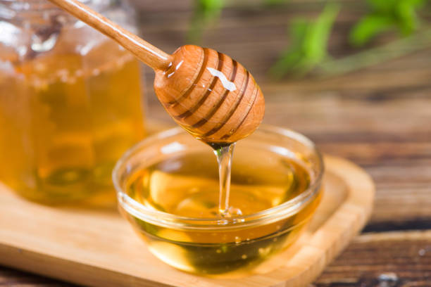 istock Honey dripping from honey dipper in glass bowl on table 1366542946