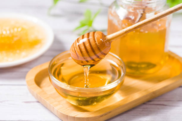 istock Honey dripping from honey dipper in glass bowl on table 1366543098