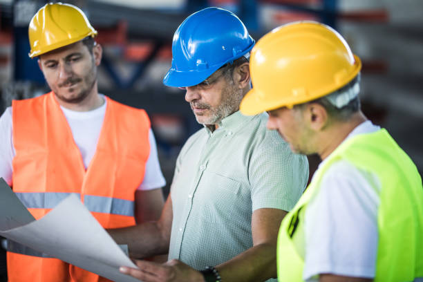 istock Manual workers and their manager cooperating while analyzing blueprints in industrial building. 1366544147
