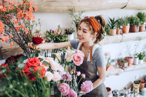 joven florista asiática, propietaria de una floristería de pequeñas empresas, que maneja y cuida flores y plantas en el lugar de trabajo. disfrutando de su trabajo de estar con las flores. concepto de pequeña empresa - i love my job fotografías e imágenes de stock