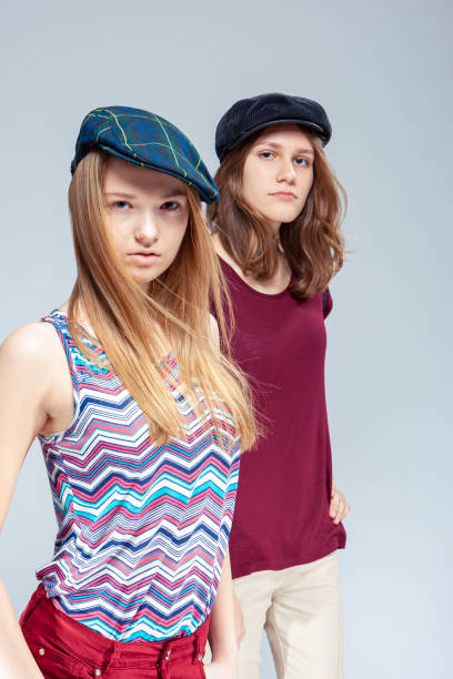 istock Modern Lifestyle. Two Blond Caucasian Girlfriends Posing Together While Wearing Caps Over White Background. 1366545885