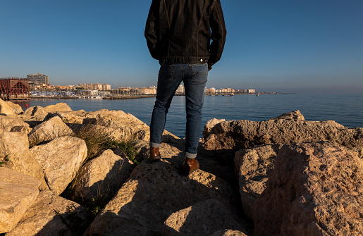 Rear view of adult man legs standing on rock with city in background. Almeria, Spain